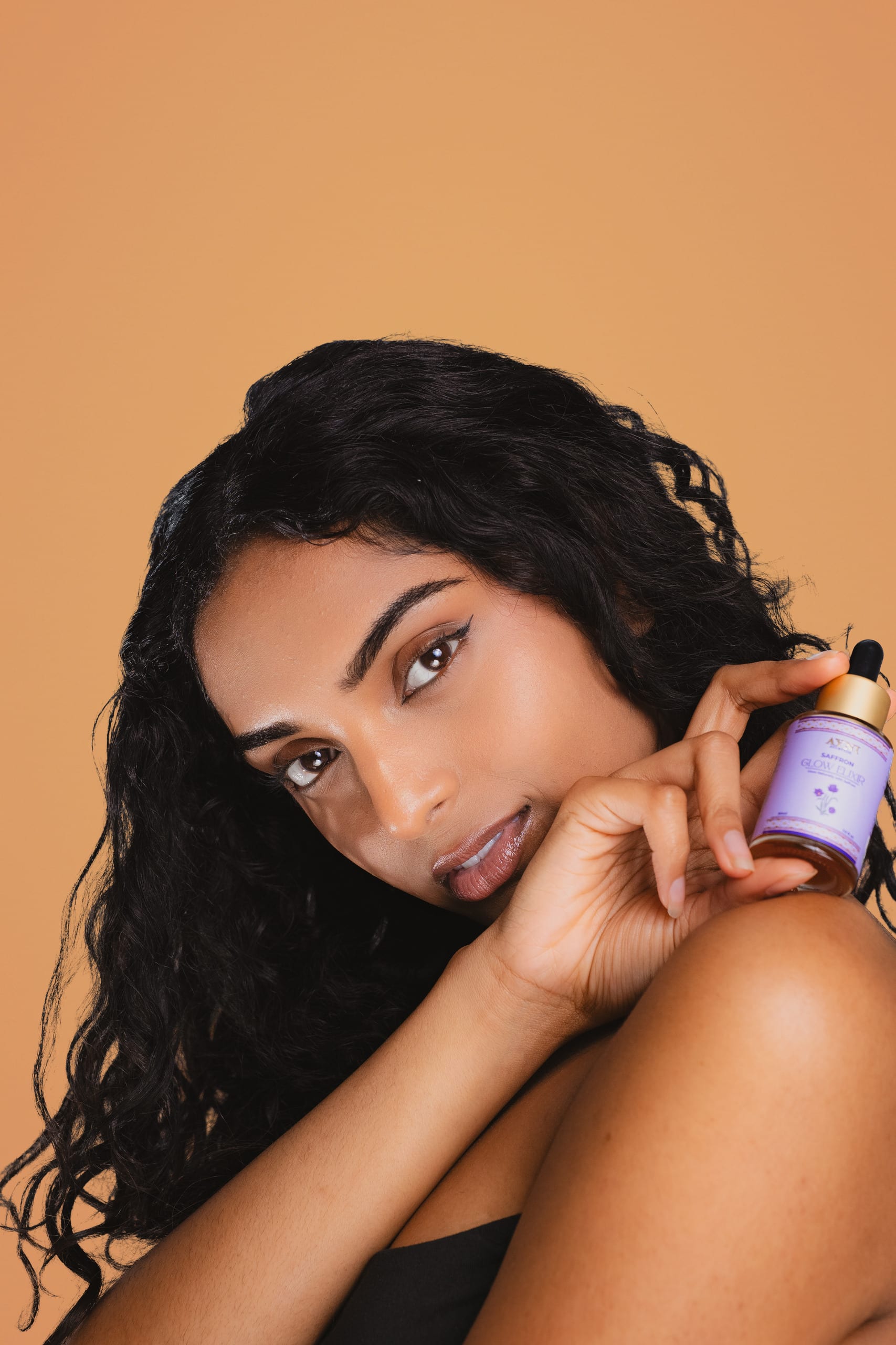 Beauty test shot resting against a glow elixir serum bottle, terracotta background