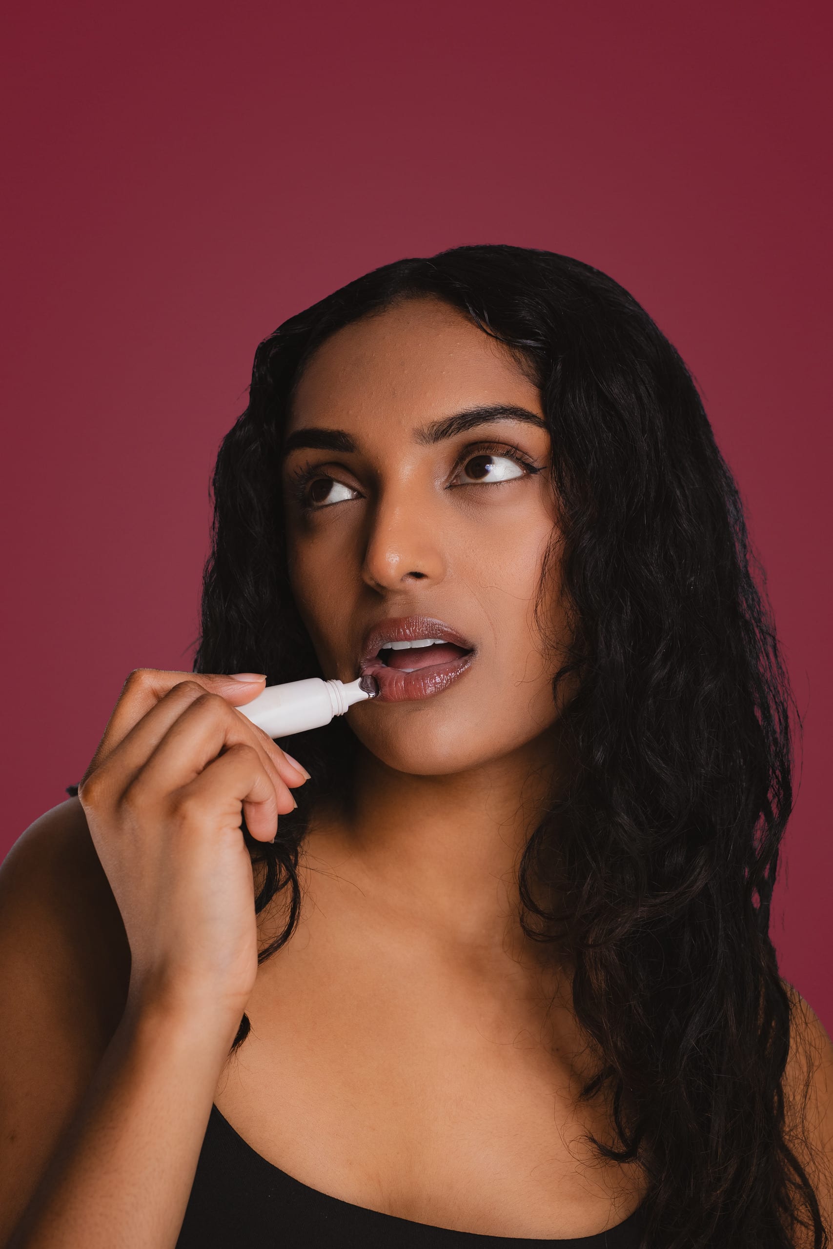 Beauty test shot applying lip gloss, burgundy background