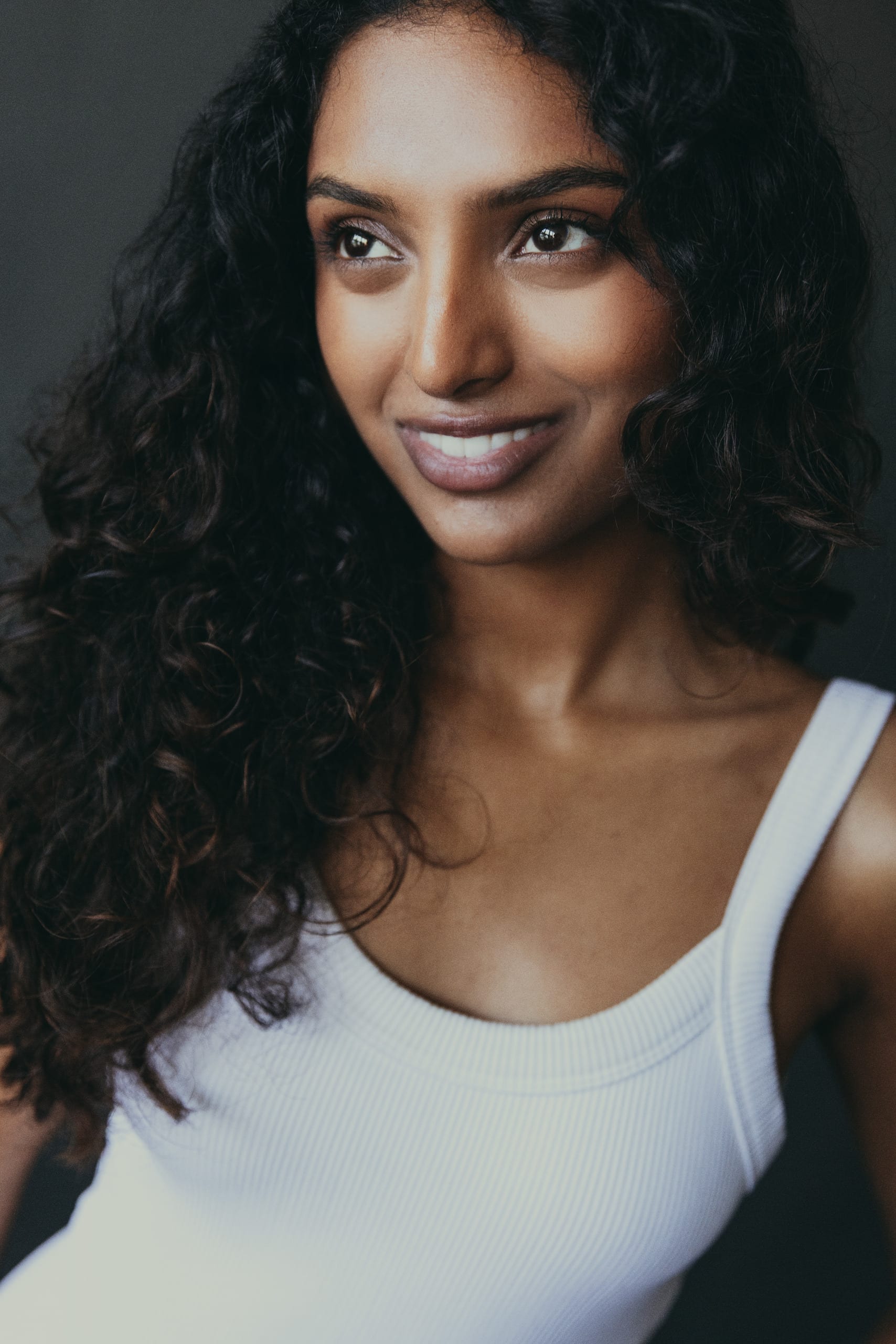 Smiling portrait in a white tank against a grey studio backdrop