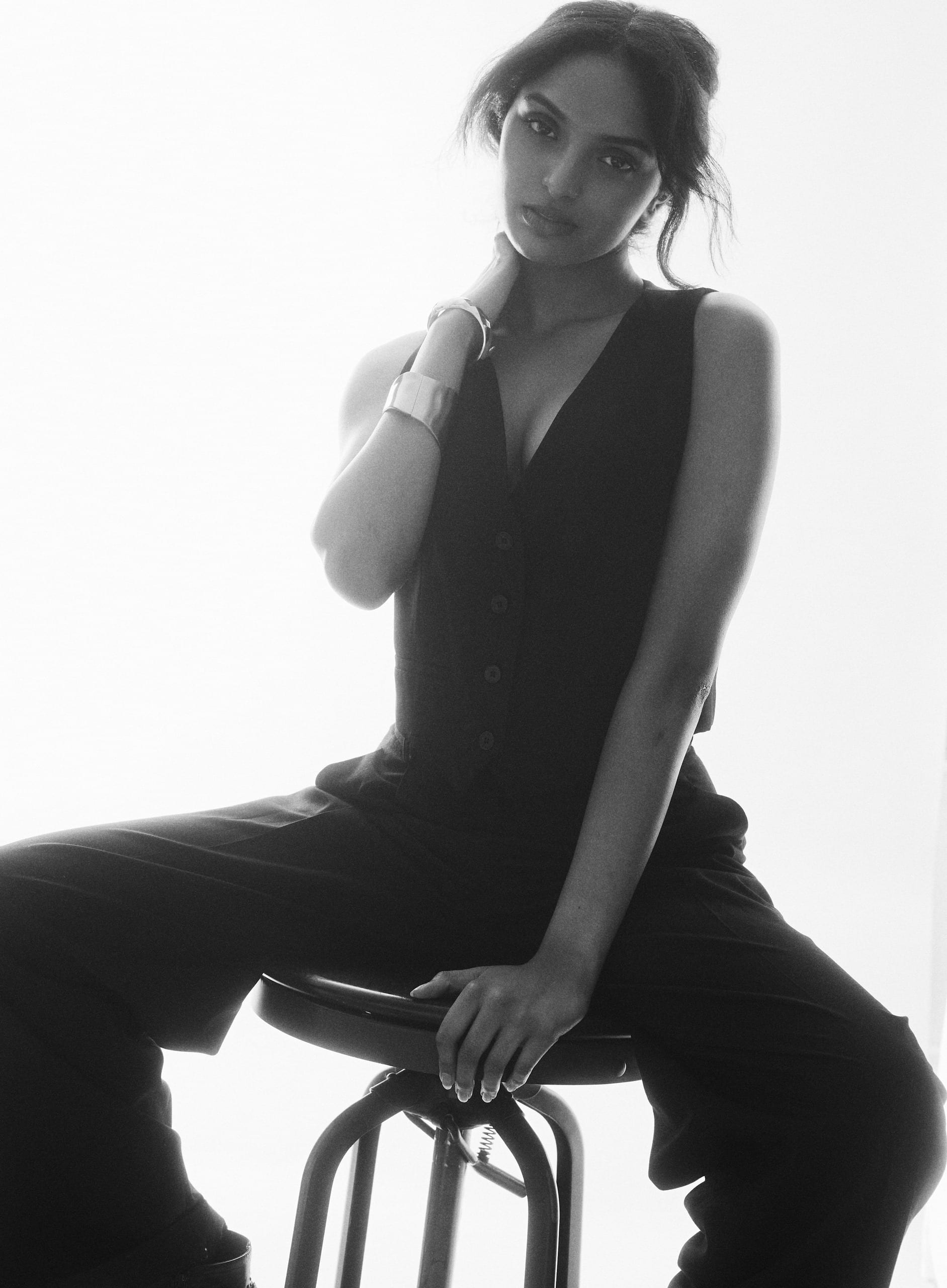 Black and white editorial, seated on a stool in a waistcoat
