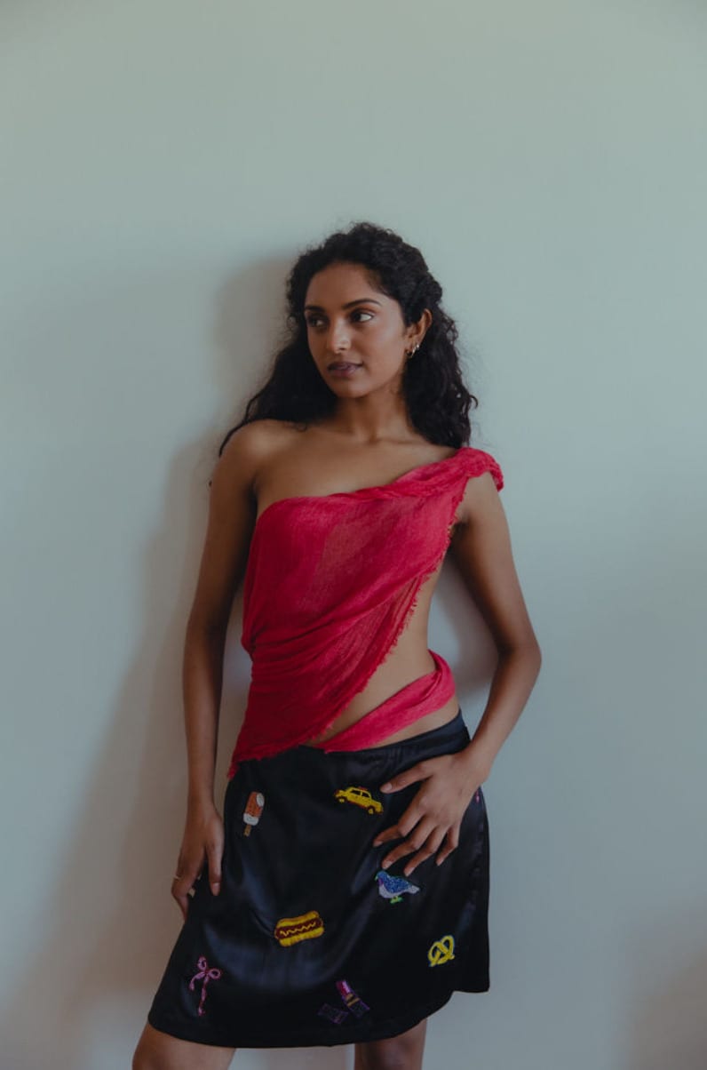 Editorial test in a draped red top and printed black skirt against a pale wall