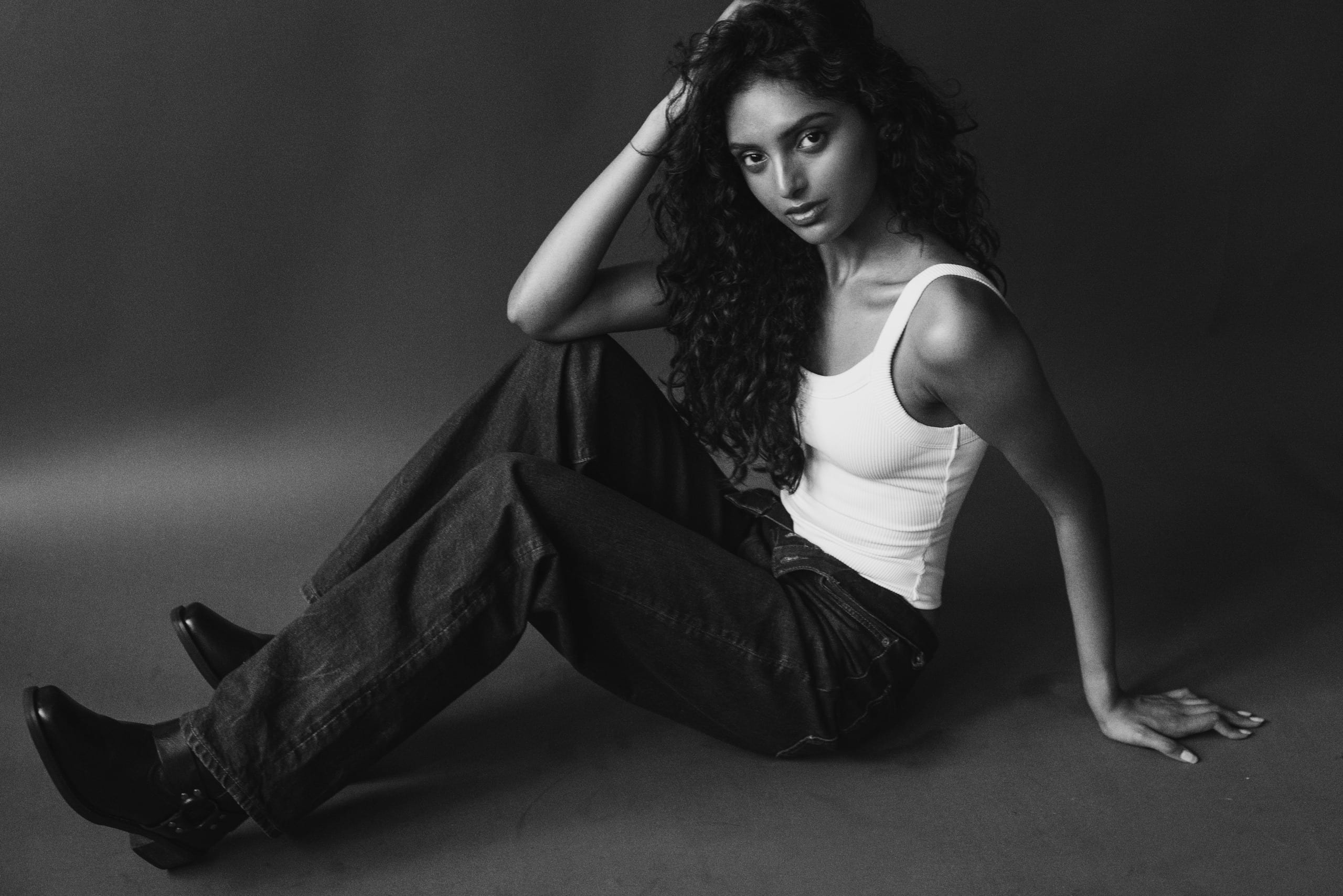 Black and white editorial, seated on the floor in a white tank and dark denim