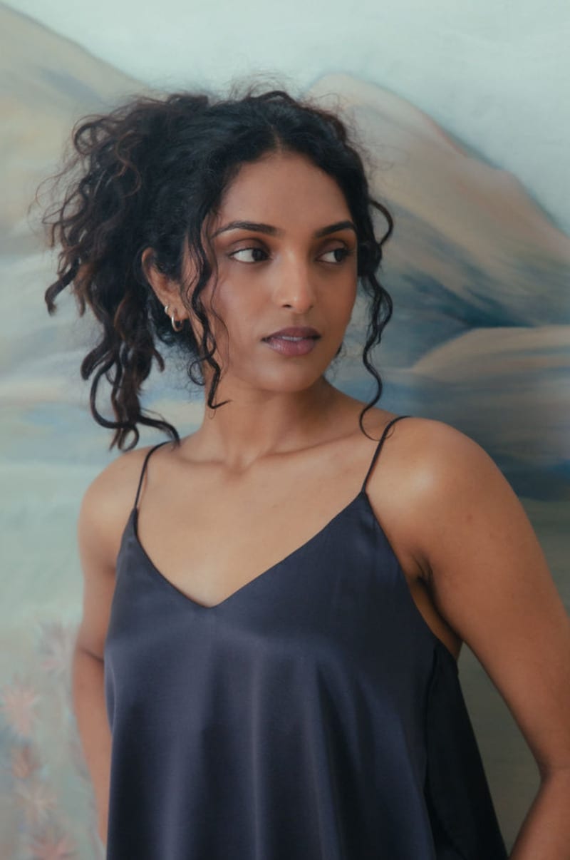 Editorial portrait in a navy slip dress against a painted landscape backdrop