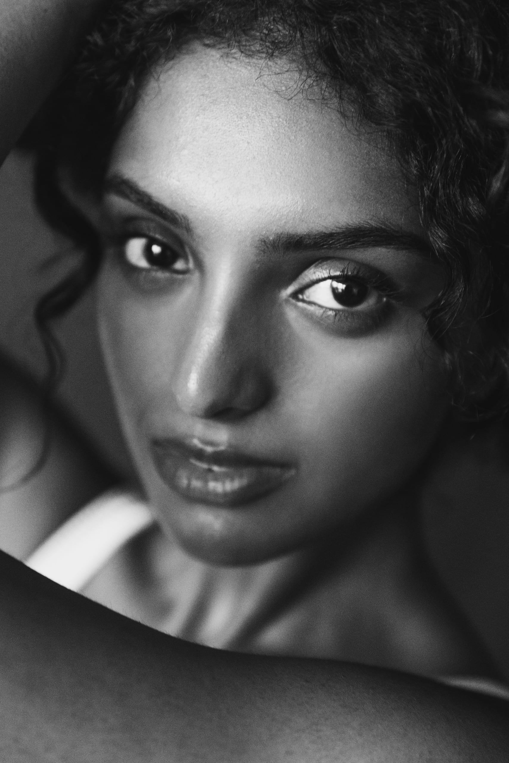 Black and white close editorial portrait, head tilted, arm across the frame