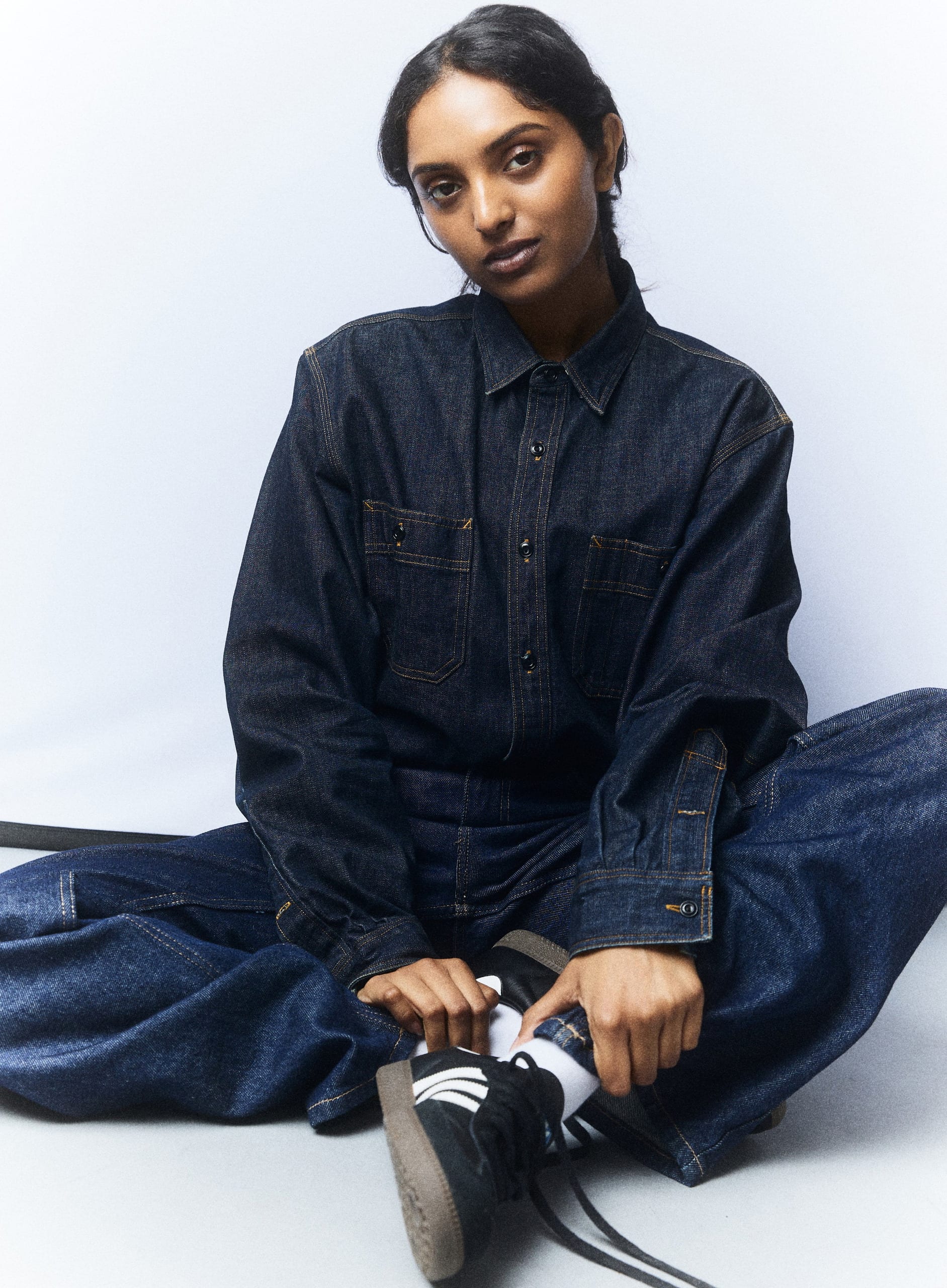 Denim on denim, seated on the floor lacing a sneaker