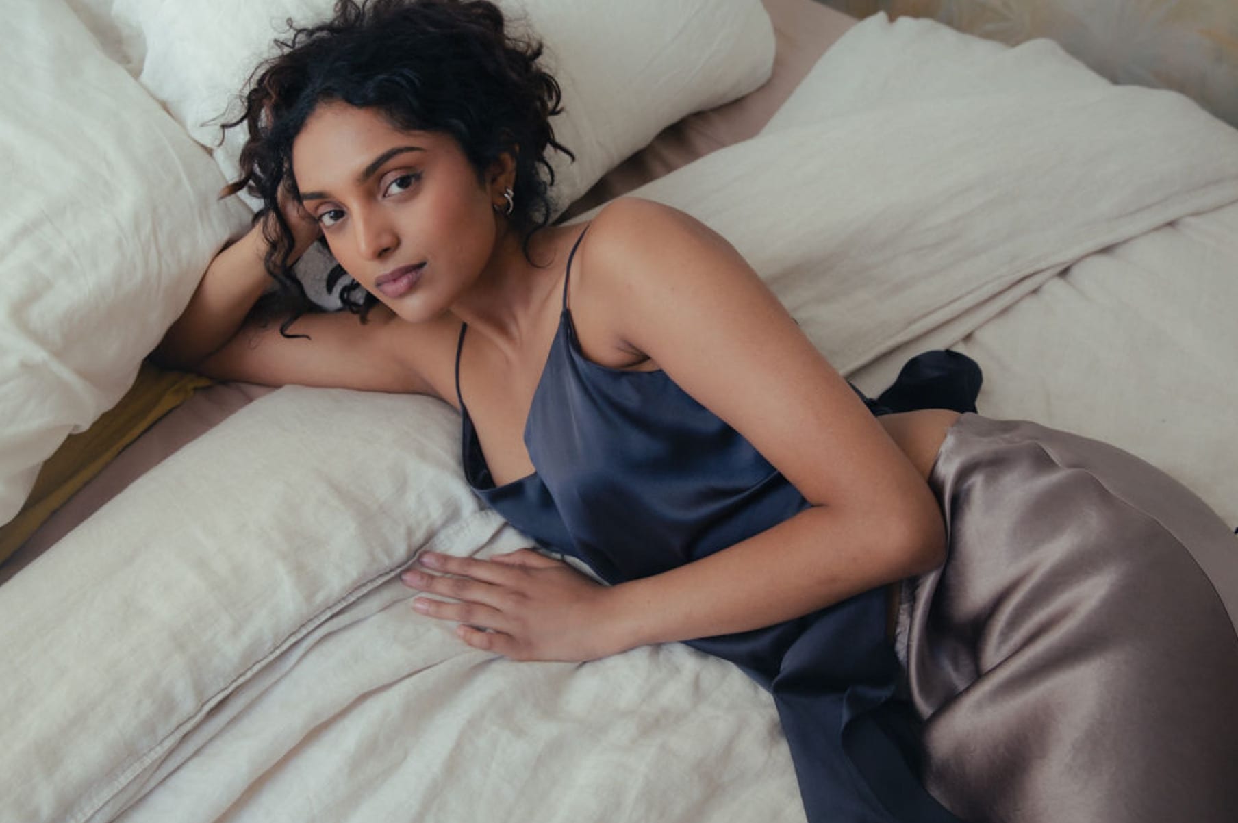 In a navy slip dress, lying across white bed linen