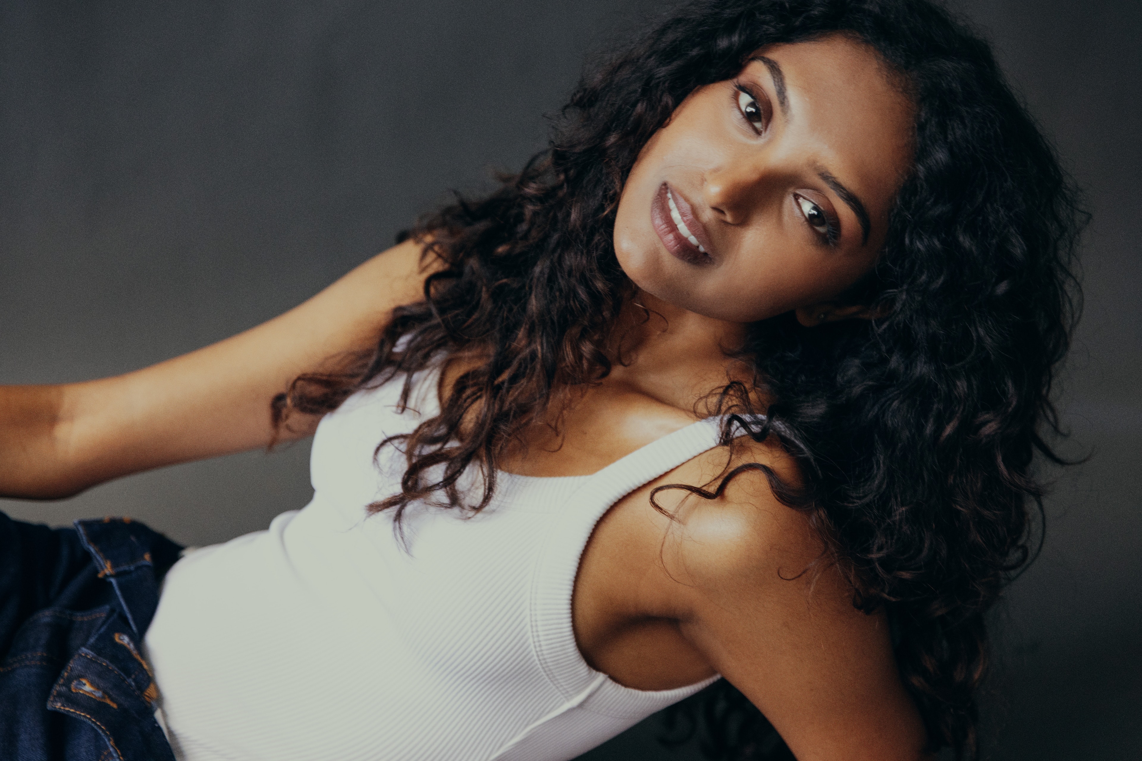 Sangavi Suresh reclining in a white tank against a grey studio backdrop