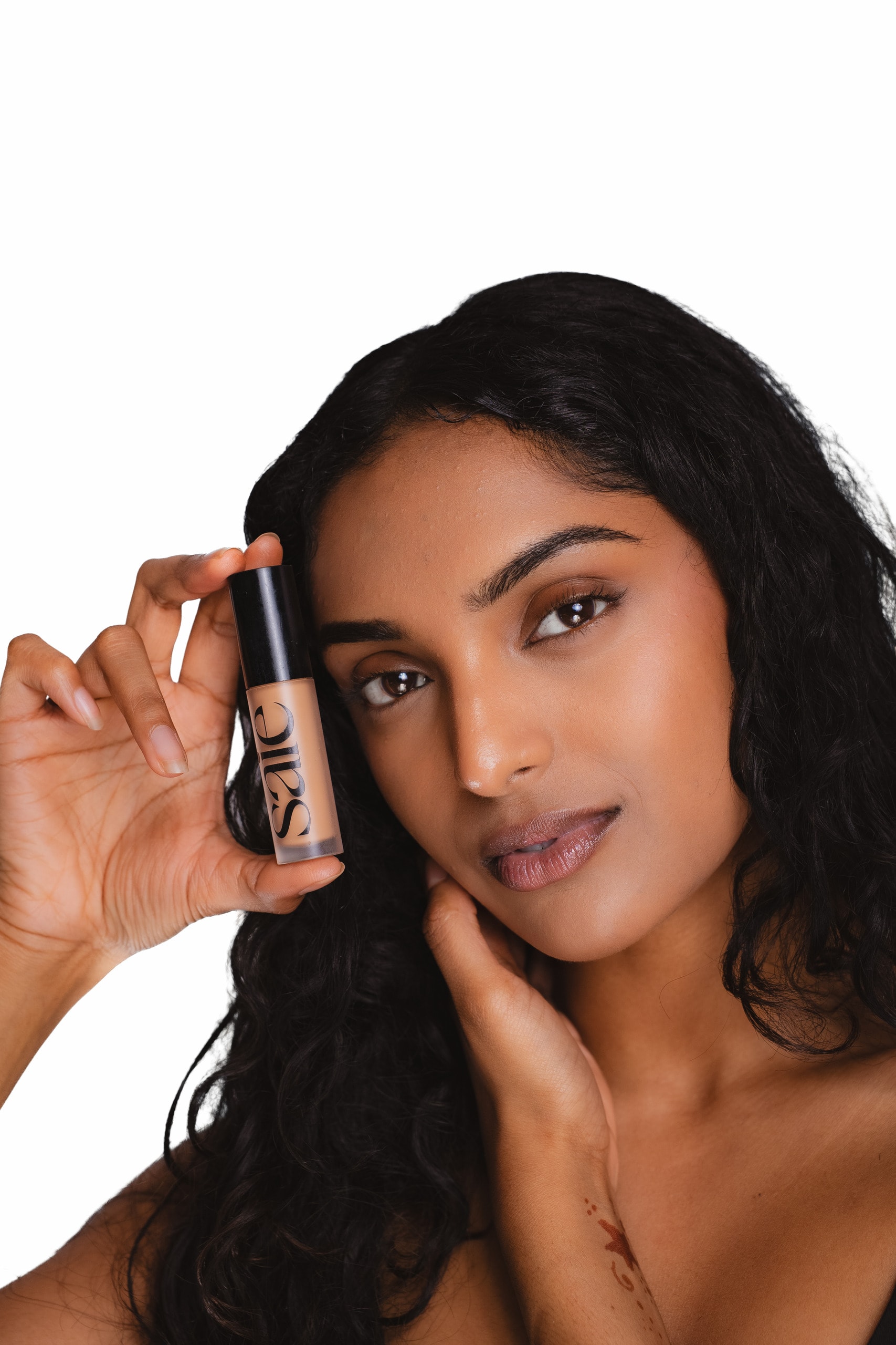 Beauty test shot holding a Saie concealer beside the face, white background