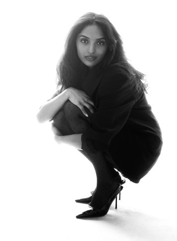 Black and white editorial, crouching in a black coat and heels against white